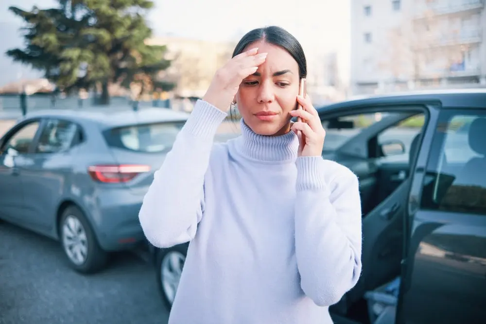 Woman Holding Her Head And Talking On The Phone Next To A Car Accident Scene